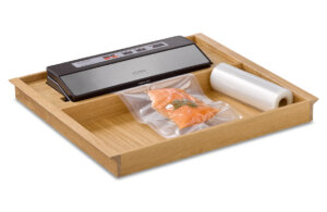 Vakuumiergerät mit Holztablett, Rolle mit Vakuumbeuteln und vakuumverpacktem Lachs mit Rosmarin